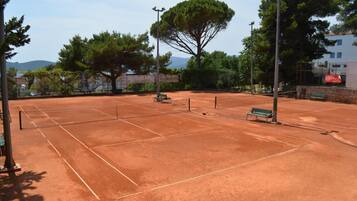Ein Tennisplatz mit Bänken, Bäumen und einer Steinmauer.