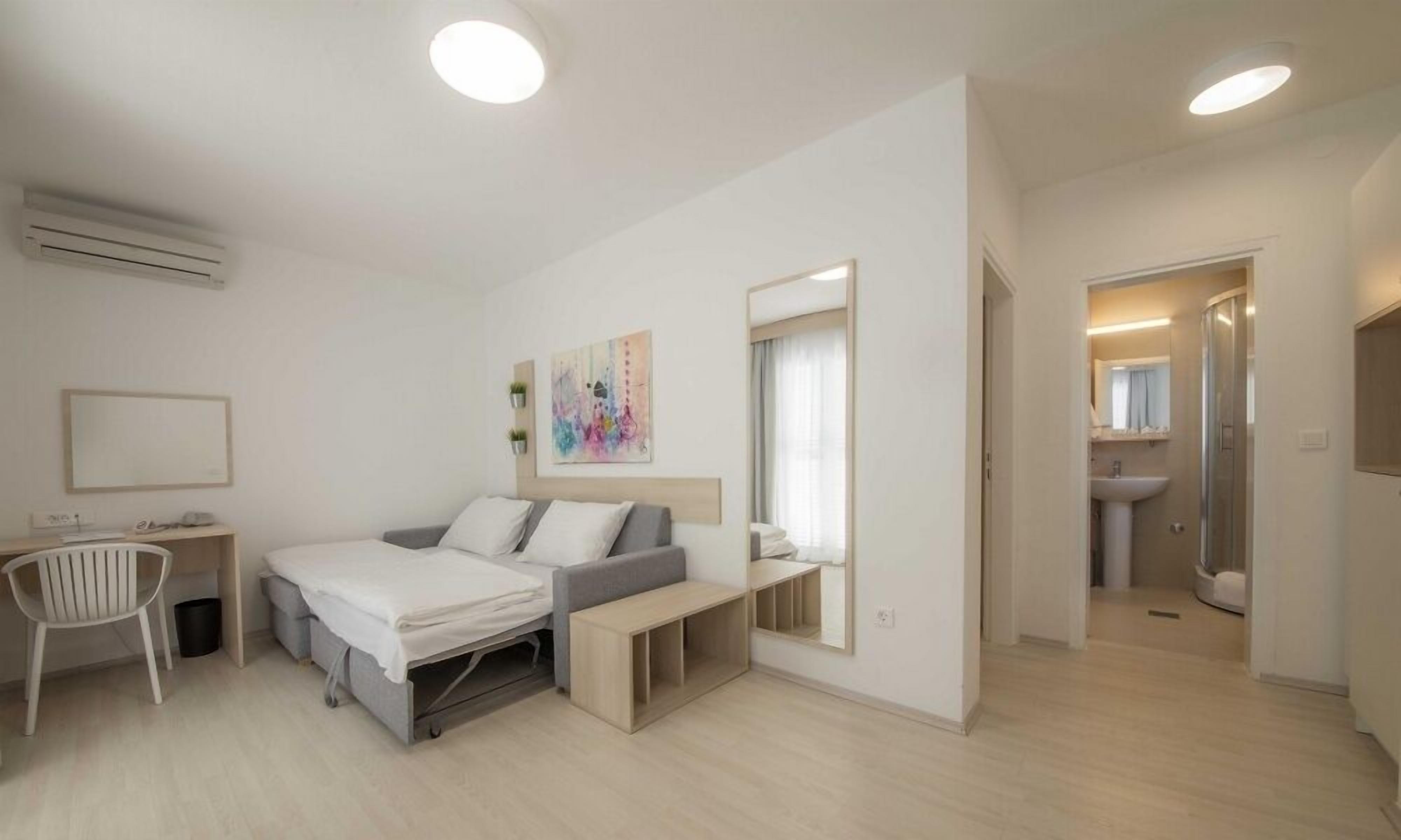Ein modernes Hotelzimmer mit einem Bett, einem Schreibtisch, einem Stuhl und einem durch eine offene Tür einsehbaren Badezimmer.