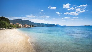 A beach with clear waters, a sandy shore, and buildings with red roofs in the background. - Bellevue Maradiso Village by Aminess  (Orebic)
