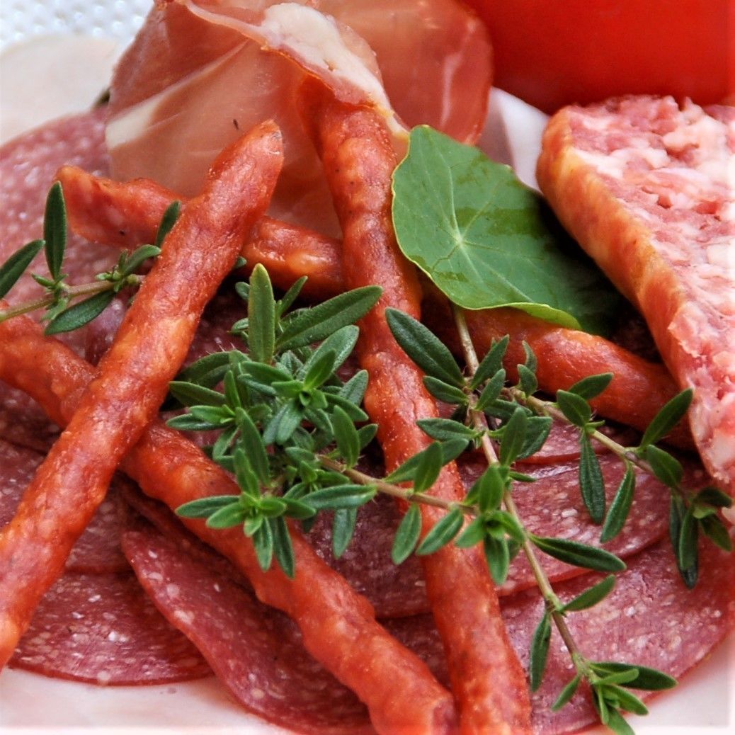 Une assiette de salami et de jambon de Parme coupés en tranches, décorée d’herbes fraîches.