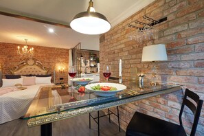 A hotel room with a brick wall, a glass dining table, a bed with a gold headboard, and a chandelier. - Strohhutmanufaktur (Dresden)