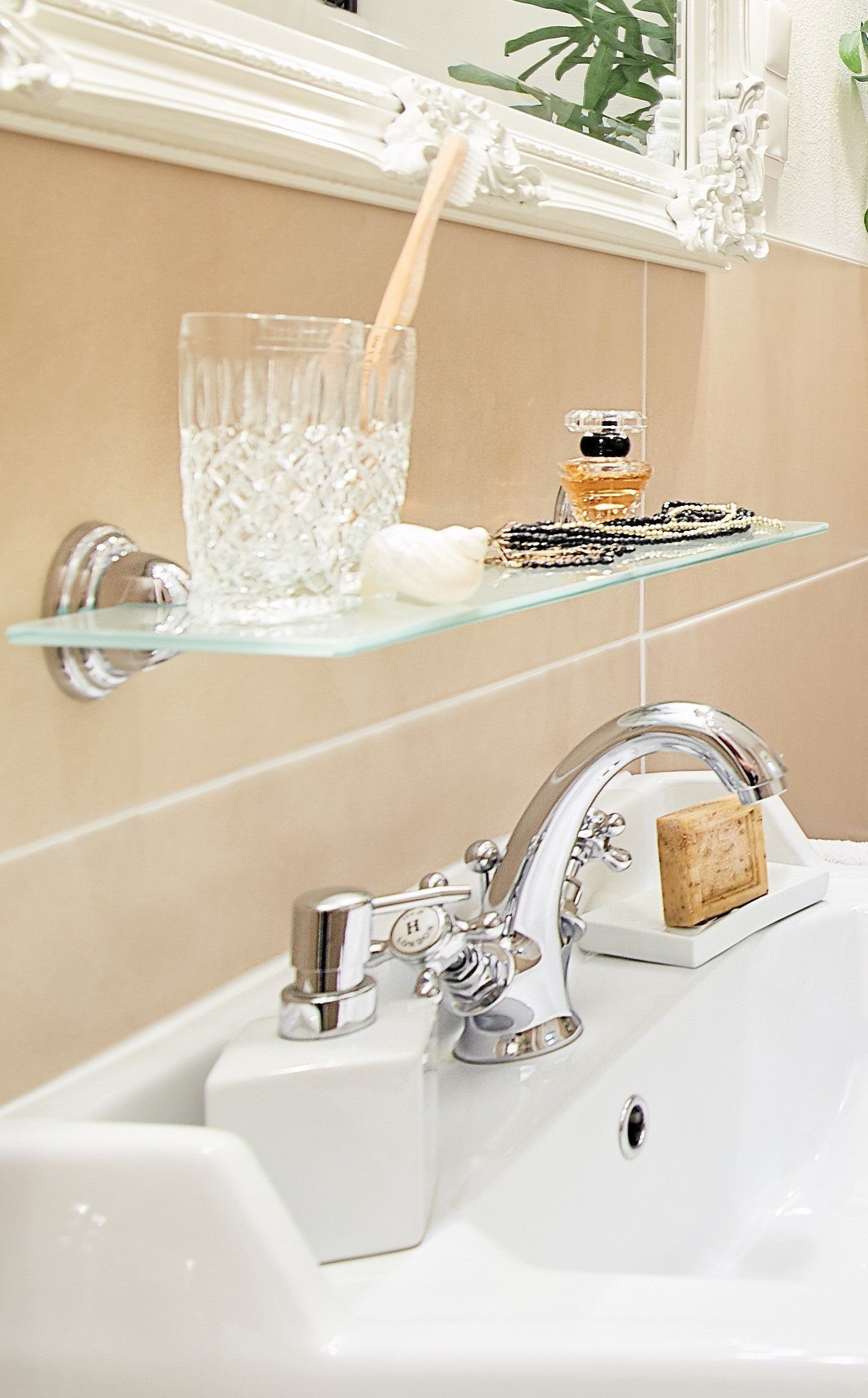 A bathroom with a glass shelf holding a glass of water, a bottle of perfume, and a bar of soap.
