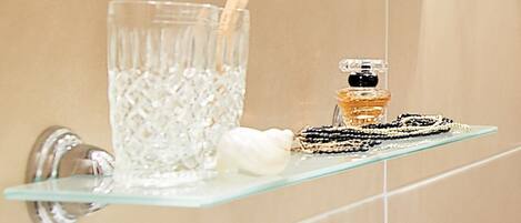 A bathroom with a glass shelf holding a glass of water, a bottle of perfume, and a bar of soap.