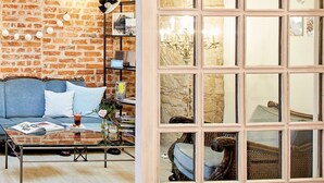 Una sala de estar con pared de ladrillo, un sofá, una mesa de centro y un ventanal con vista a una estatua.