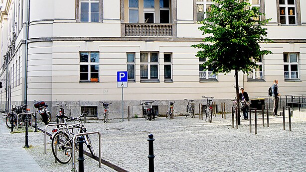 Un edificio histórico con un balcón destacado, un letrero de estacionamiento a la vista y bicicletas estacionadas afuera.