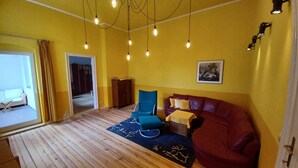 Una habitación con piso de madera, un sofá de cuero rojo, un sillón azul y un tapete estampado.