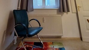 Una habitación con ventana, una silla, un radiador y una alfombra colorida.