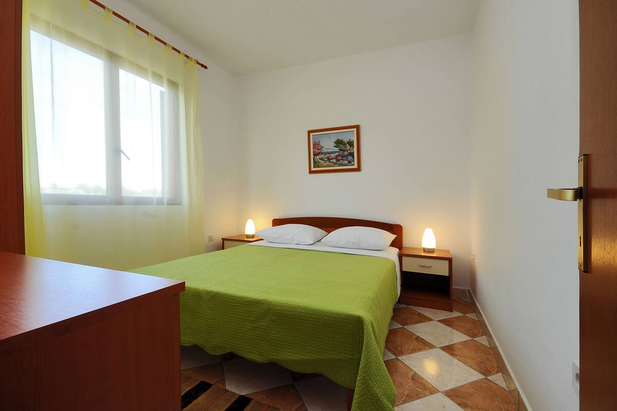 A bedroom with a bed, bedside lamps, a wooden desk, and a window with curtains.