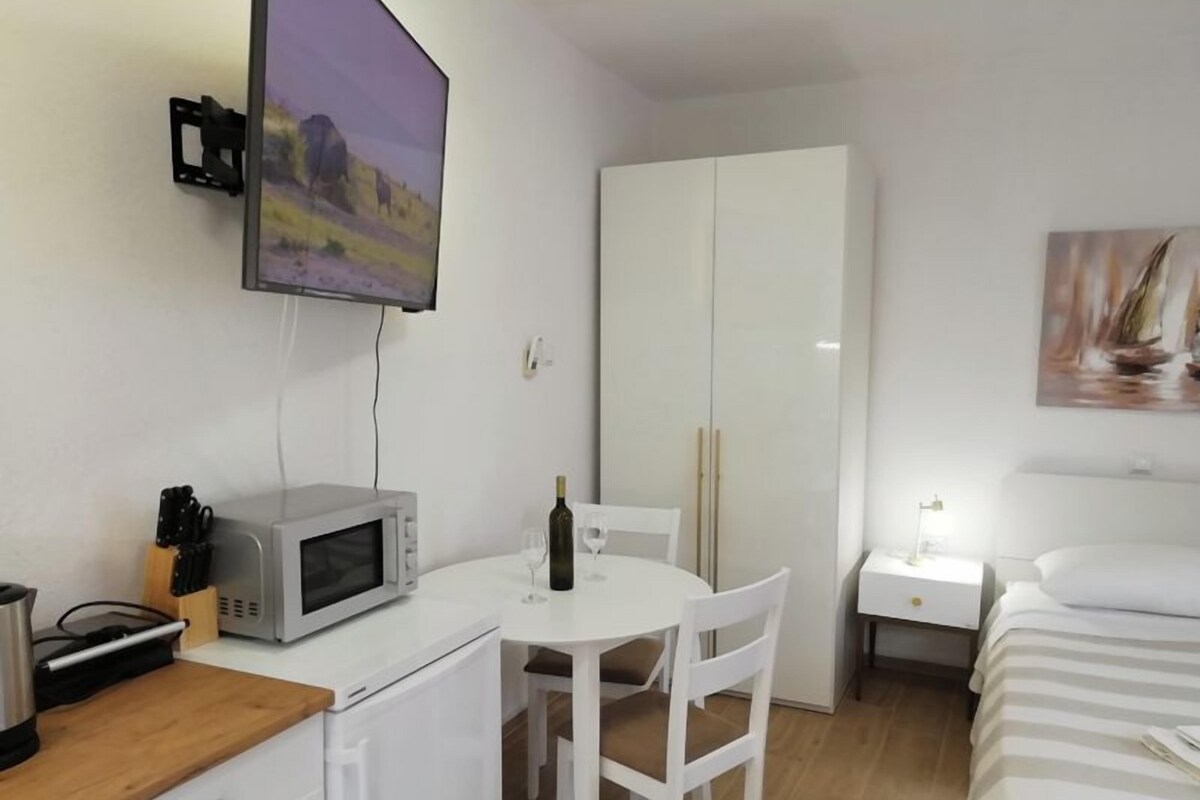 A compact room with a bed, a desk with a computer, a microwave, and a TV mounted on the wall.