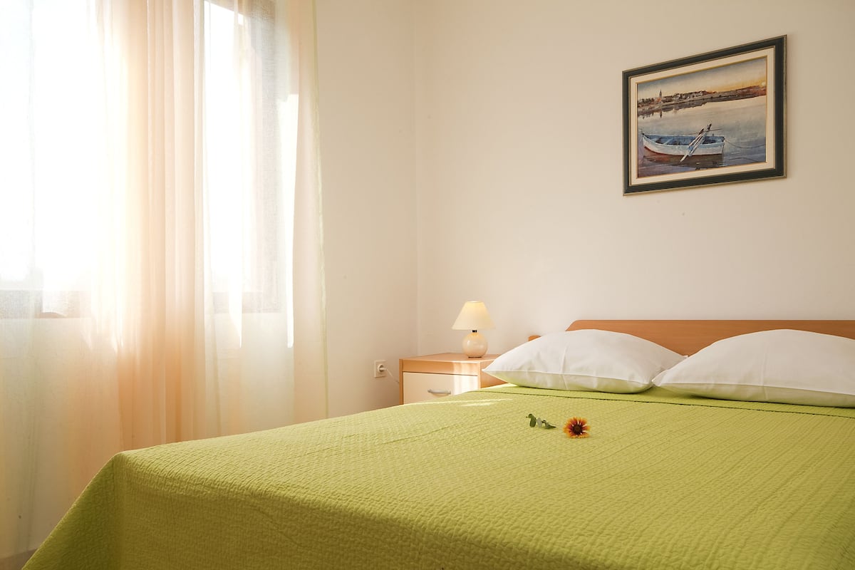 A hotel room with a bed, a nightstand, a lamp, and a painting on the wall.