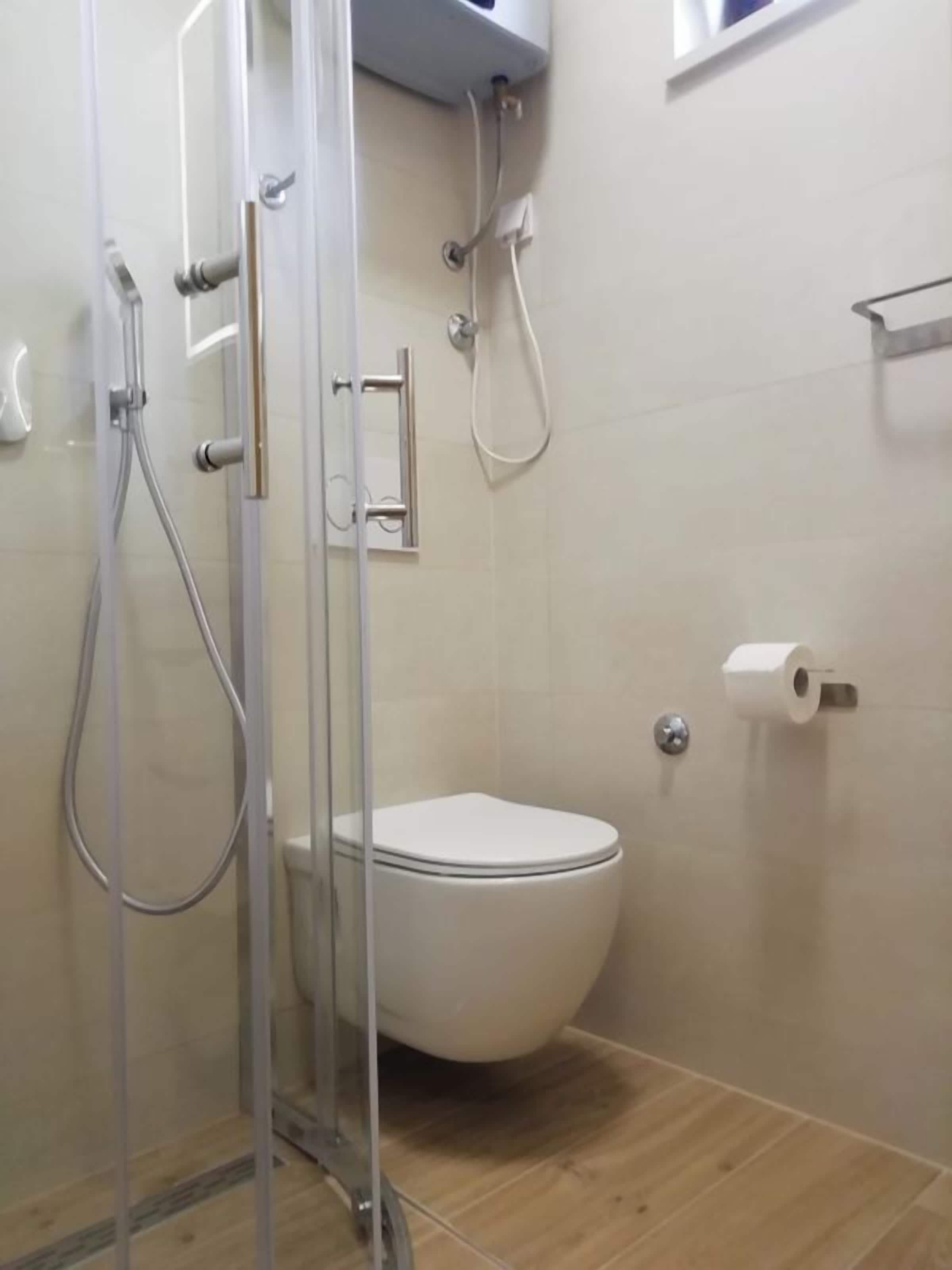 A bathroom with a toilet, a shower enclosure, and a toilet paper holder.