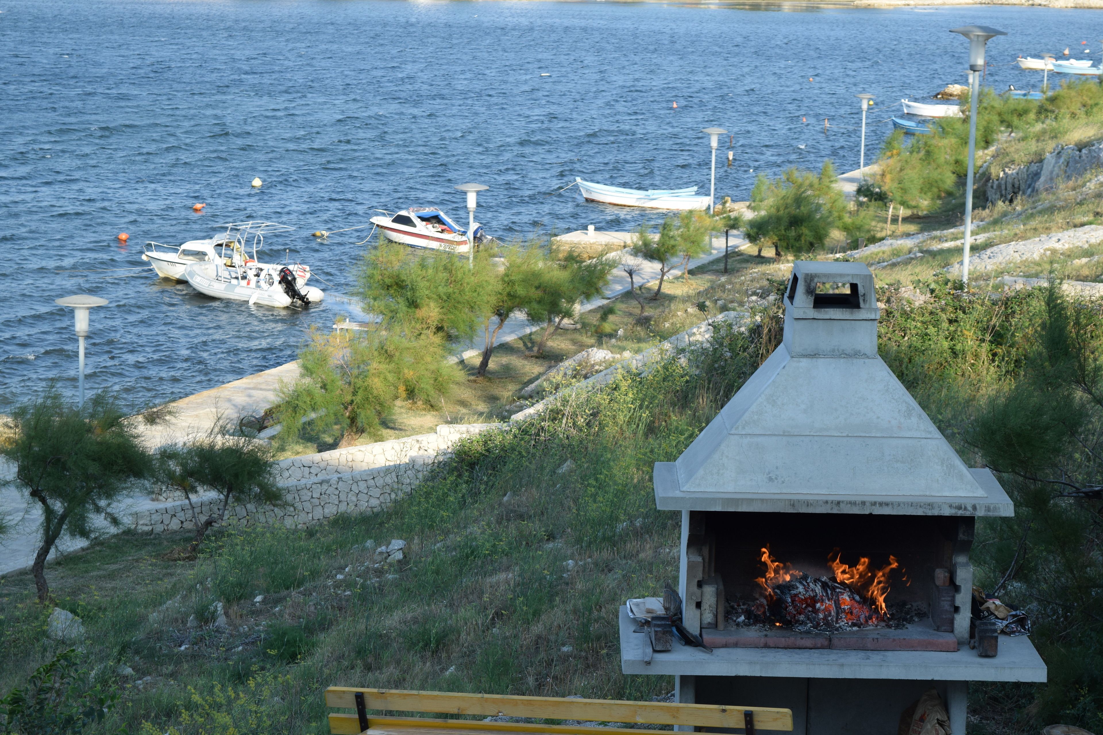 Utsikt över vattnet med båtar, en grill och en stenmur.