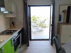 A kitchen with a gas stove, oven, and green cabinets. There is a sliding glass door leading to an outdoor seating area with chairs. - Apartments Valentina-B (Nin)