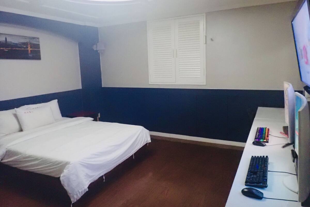 A hotel room with a bed, a desk with a computer, and a window with blinds.