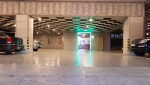 A parking garage with a checkered ceiling, a neon sign, and a few parked cars. - Provence Hotel (Incheon)