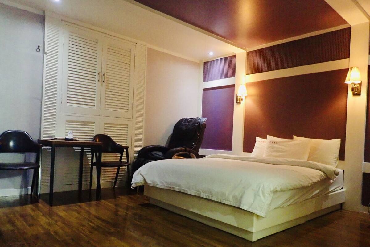 A hotel room with a bed, a desk, a chair, and a wardrobe.