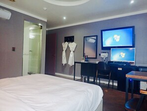 Une chambre d’hôtel avec un lit, un bureau équipé d’un ordinateur, une télévision et une robe accrochée au mur.