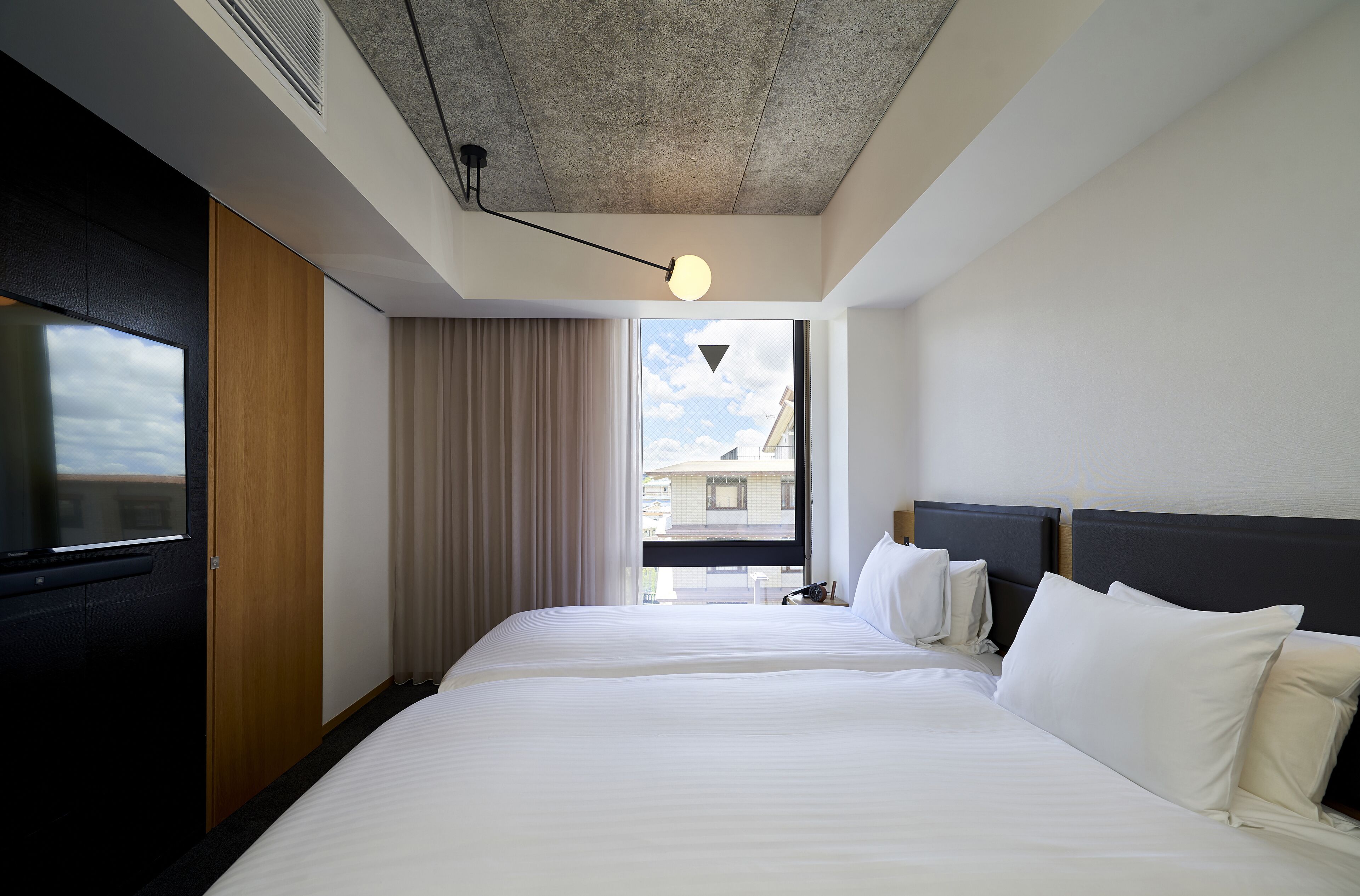A hotel room with a large bed, a TV, a wardrobe, and a view of the city.