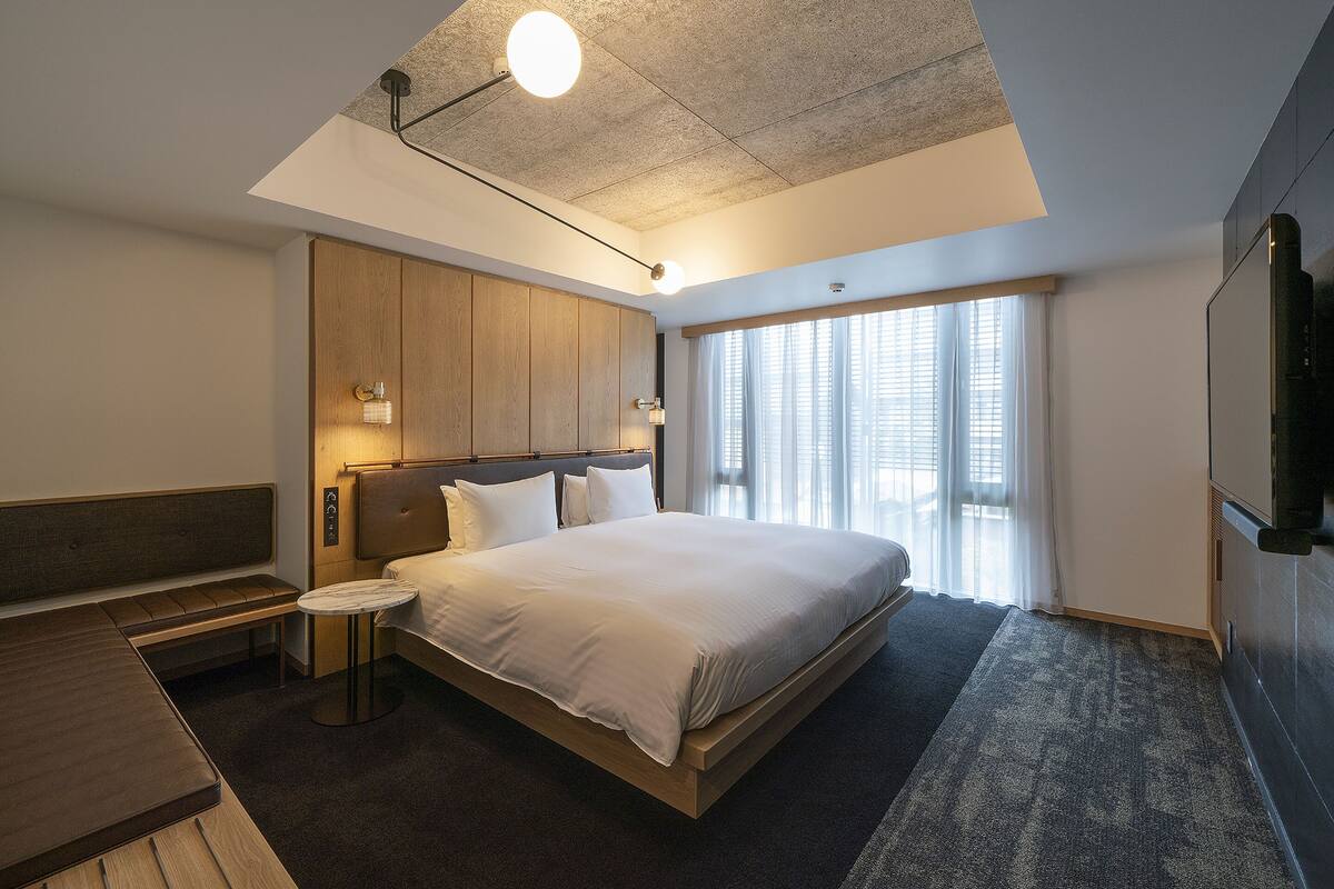 Una habitación de hotel moderna con una cama grande, un banco, una mesita pequeña y un televisor.