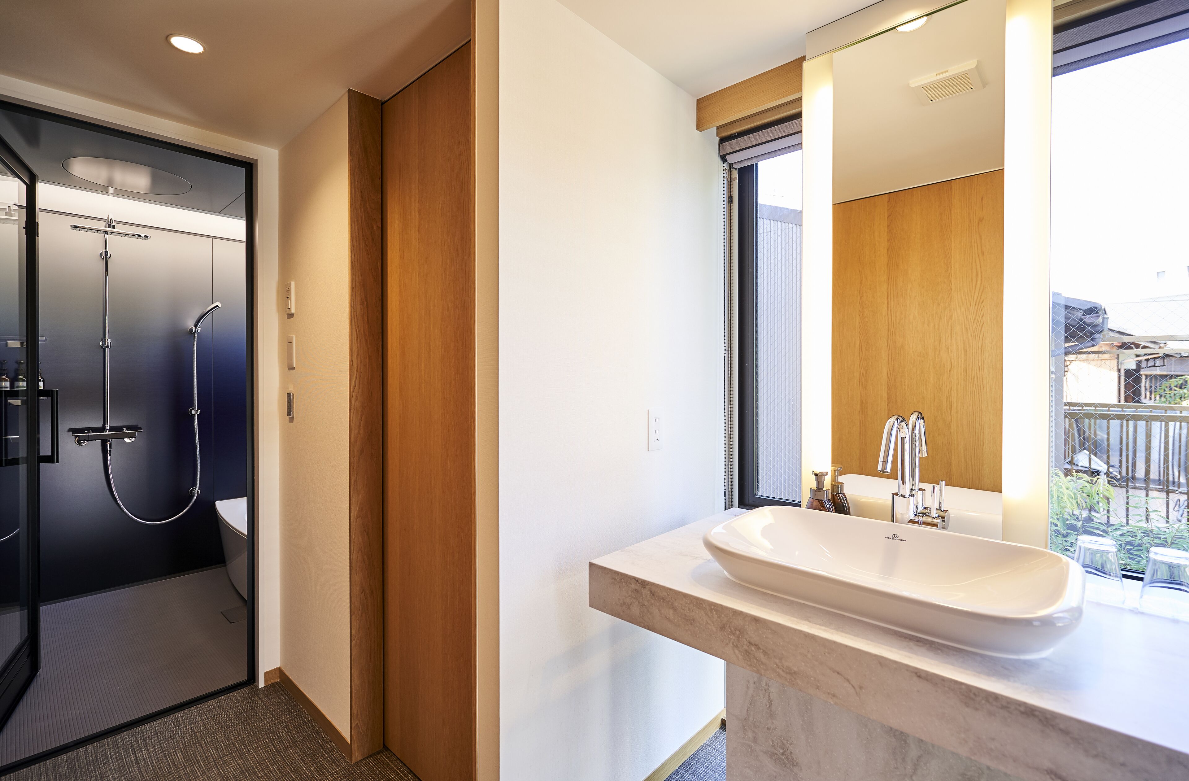 A modern bathroom with a glass-enclosed shower, a large sink with a mirror, and a view of the outside.