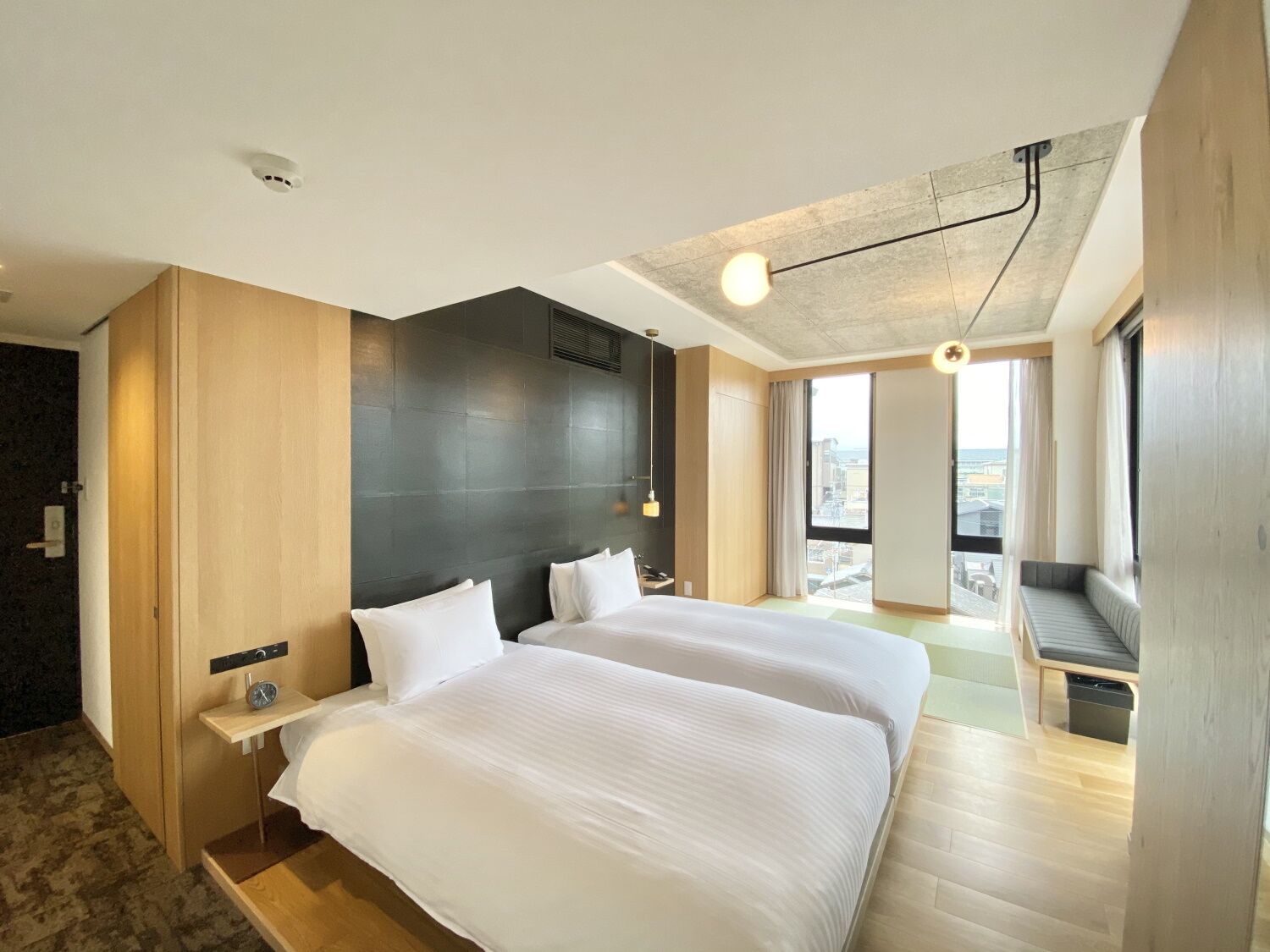 A modern hotel room with two beds, a large window, a balcony, and a city view.