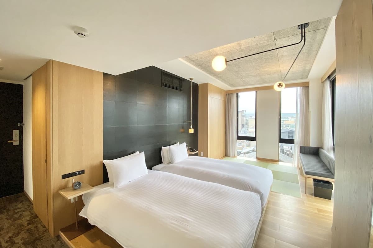 Una habitación de hotel moderna con dos camas, un ventanal grande, balcón y vistas a la ciudad.