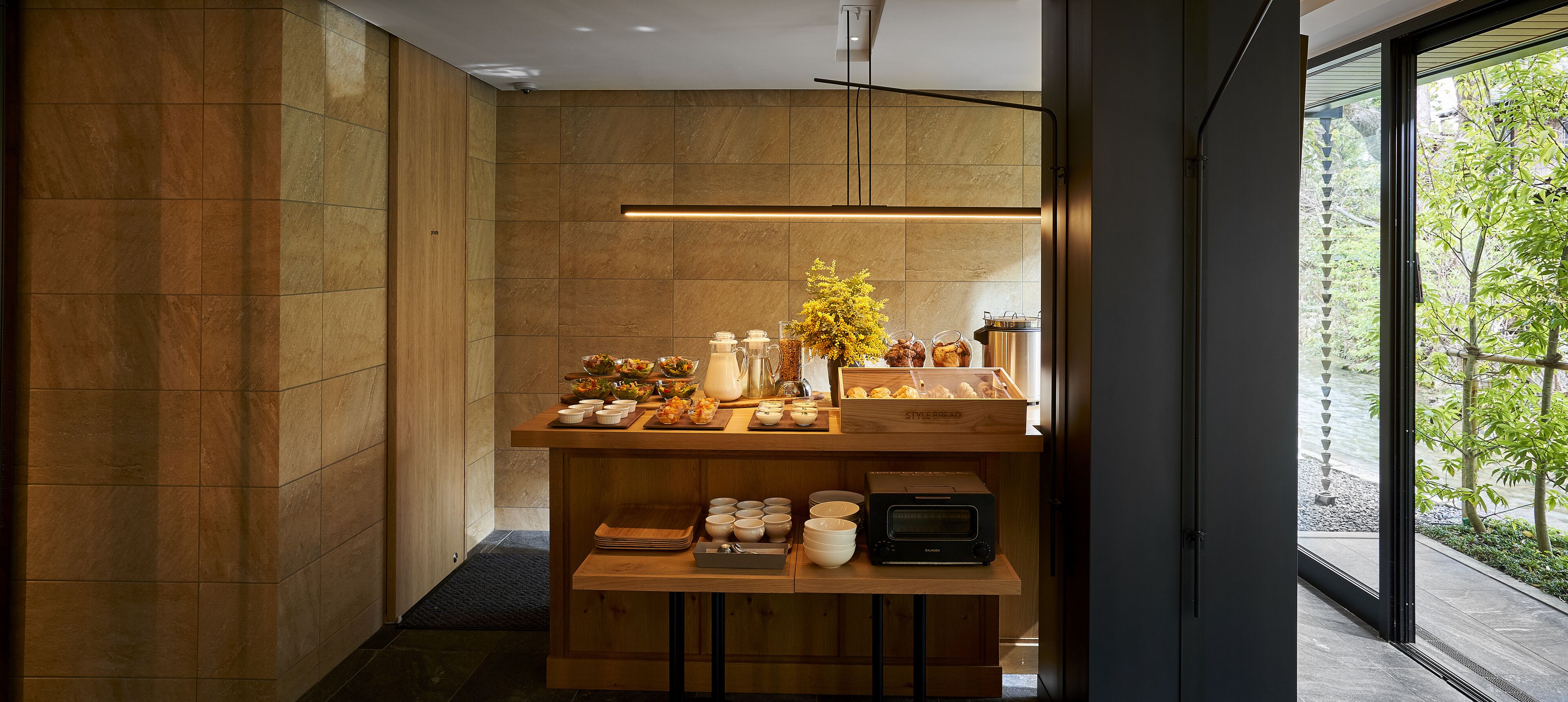 A modern kitchen with a wooden countertop, a coffee machine, and a view of a garden through a large window.