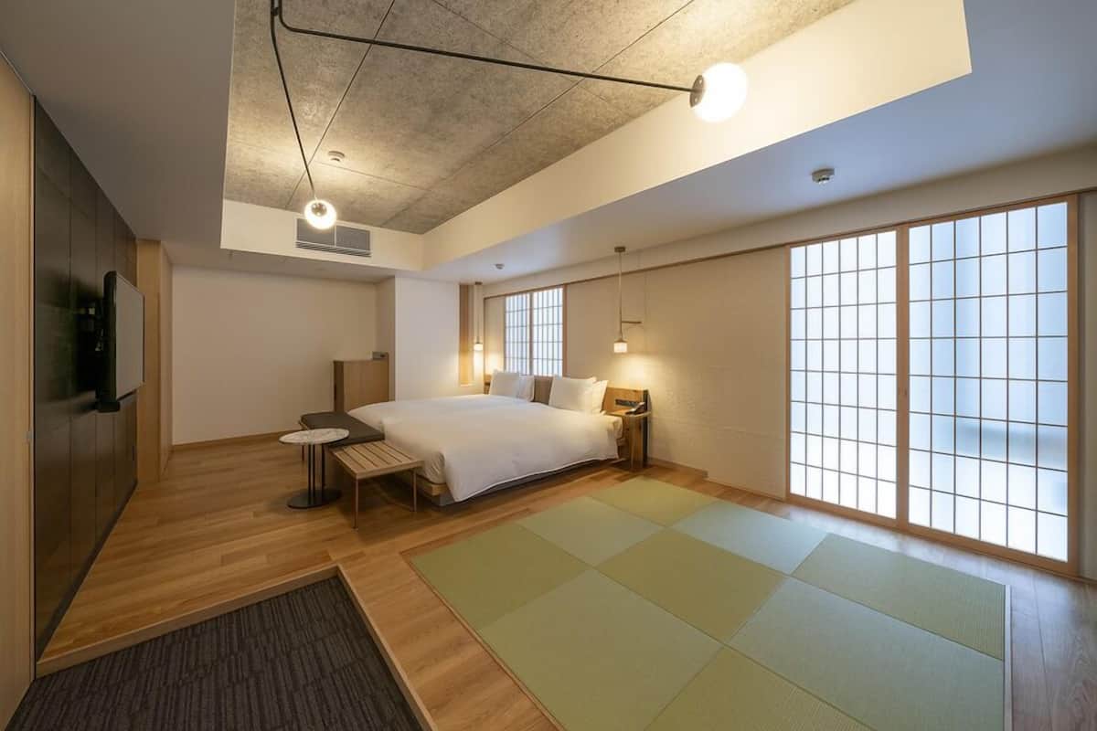 A modern hotel room with a large bed, a small table, a TV, and sliding doors.