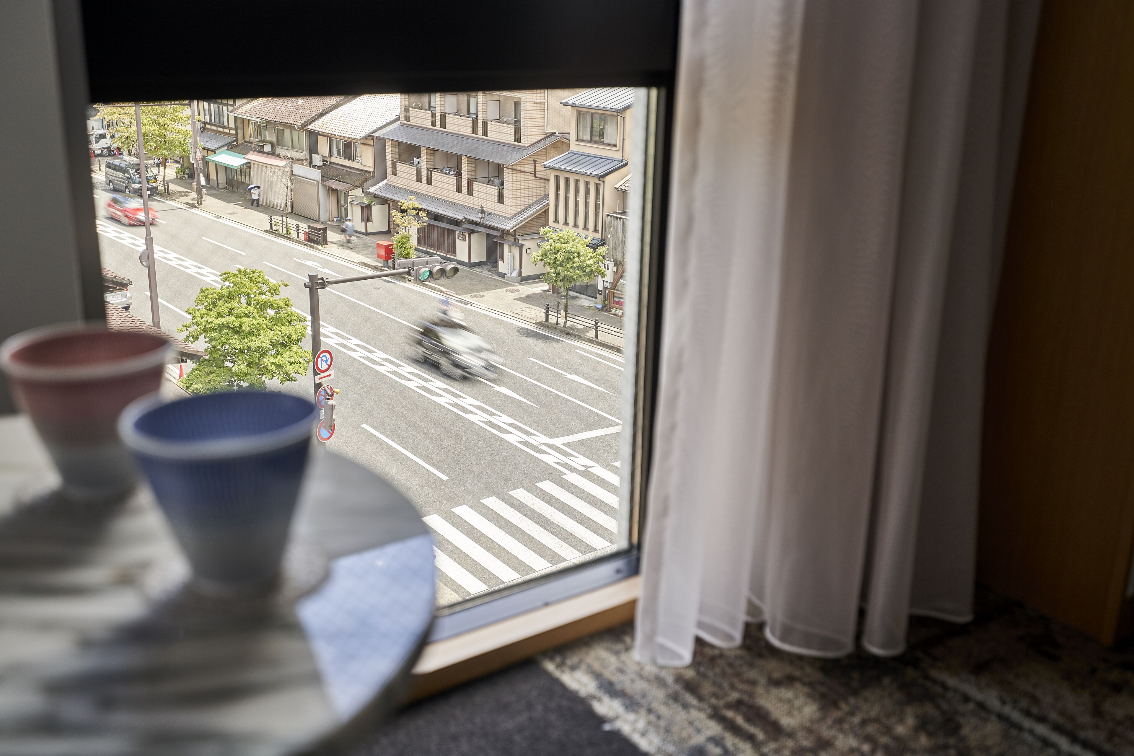 A window view of a street with buildings, a crosswalk, and a moving vehicle.