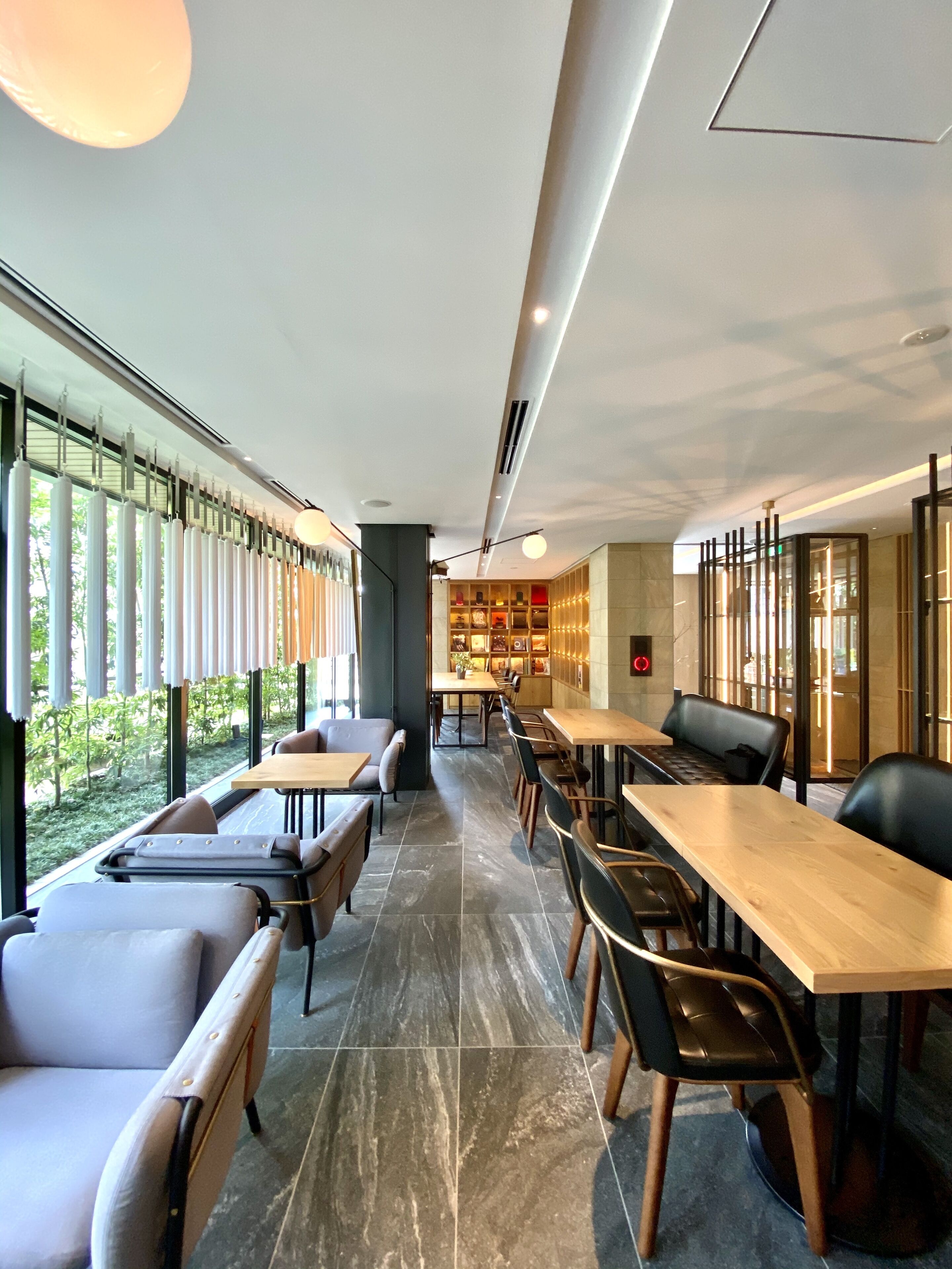 A modern restaurant with a long counter, cushioned seating, and large windows offering a view of greenery.