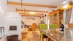 Un salon chaleureux avec une table à manger au plateau en verre, des poutres apparentes, une cheminée et un canapé vert.