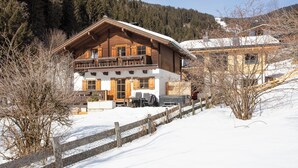 Un chalet en bois à deux étages, doté d’un balcon, entouré de neige et d’arbres.
