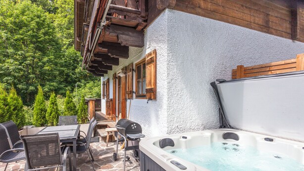 Une terrasse dotée d’un jacuzzi, d’un revêtement de sol en pierre et de mobilier en bois.
