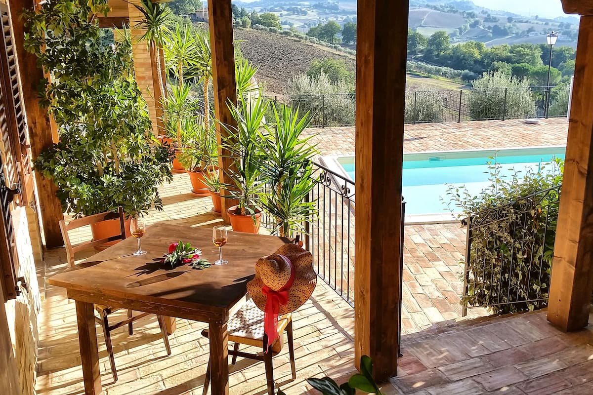 Um deck de madeira com mesa e cadeiras, com vista para uma piscina e uma paisagem deslumbrante.