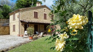 Una casa de piedra con porche, un jardín de flores amarillas y un camino de entrada de grava.