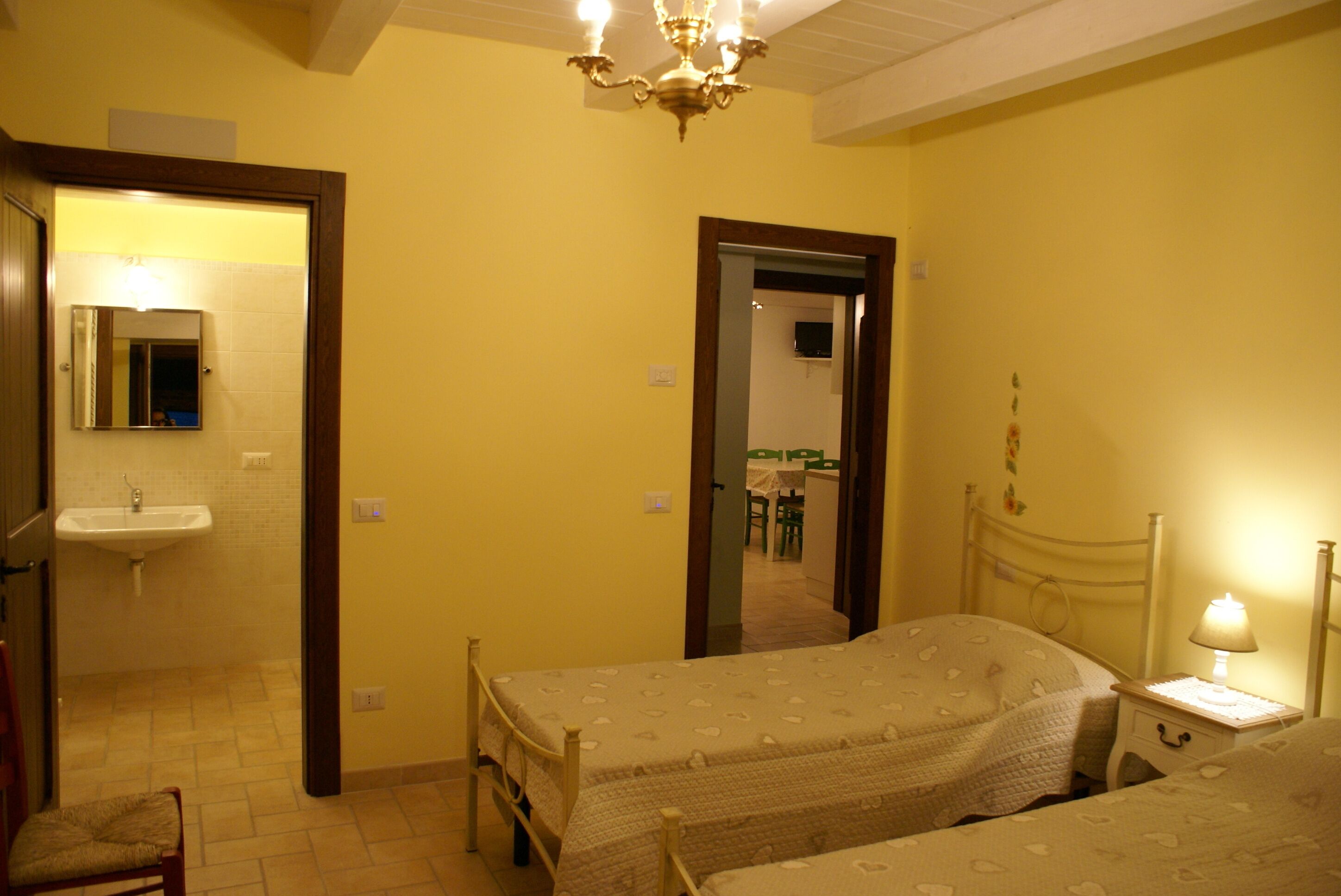A bedroom with two beds, a bedside table with a lamp, a mirror, and a door leading to a bathroom.