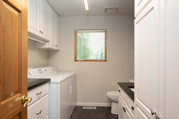 A compact bathroom with a washer and dryer, a toilet, and a window. - Private Pond, Starlink, Creekside, Firepit, Pets! (Durango)