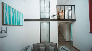 A spacious living area with a high ceiling, a large window, and a modern staircase.