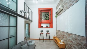 A modern living room with a grey sofa, two bar stools, a wooden bench, and a red-framed window with a view of the outside. - Shanghai Rainbow No.35 (Shanghai)