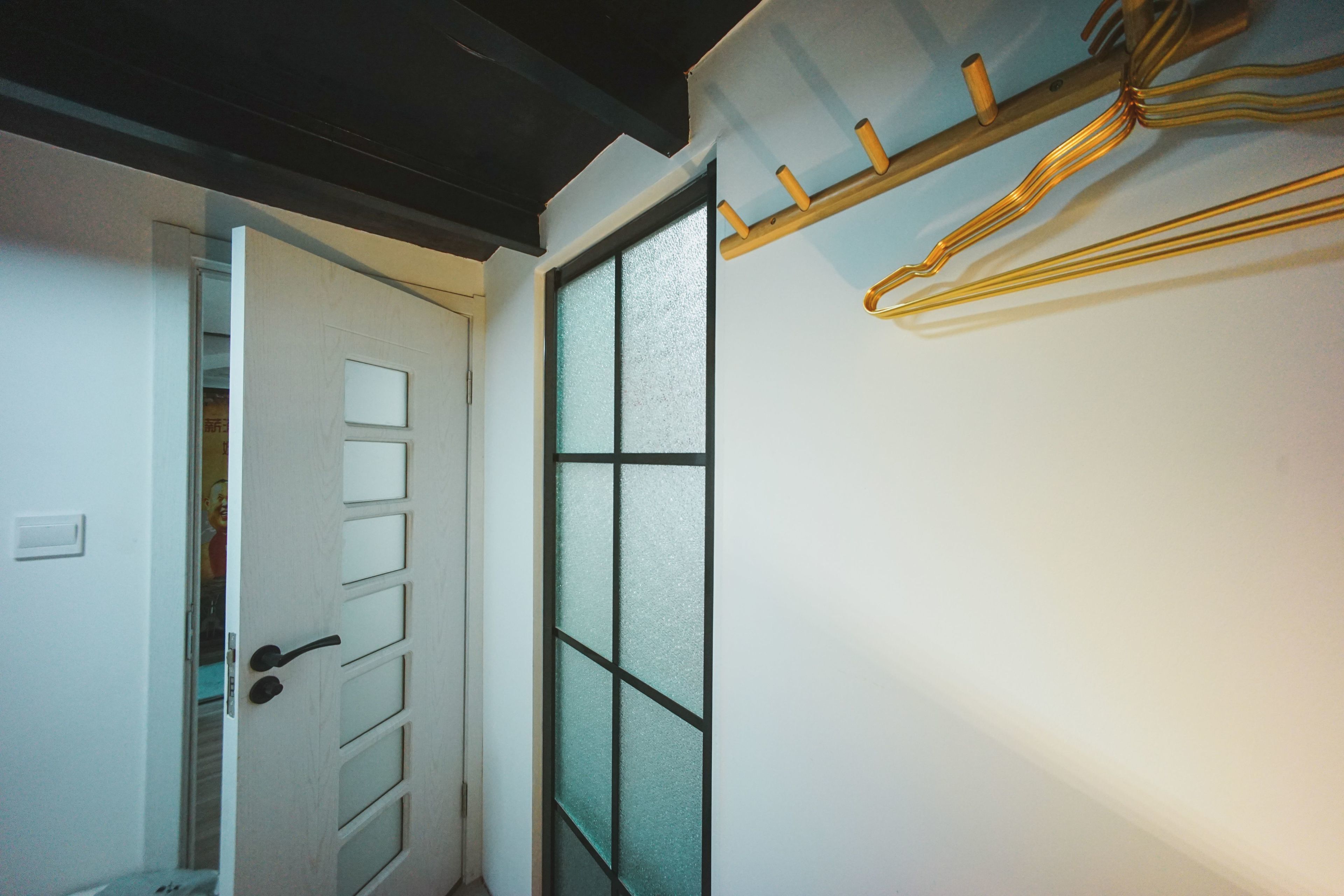 A hallway with a door leading to a room, a frosted glass window, and a coat rack with hangers.