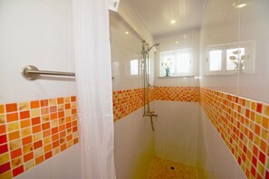 Ducha con puerta de vidrio, barra de apoyo y pared de azulejos con una ventana arriba.