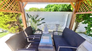 En udendørs patio med fletmøbler, et lille bord og en statue.