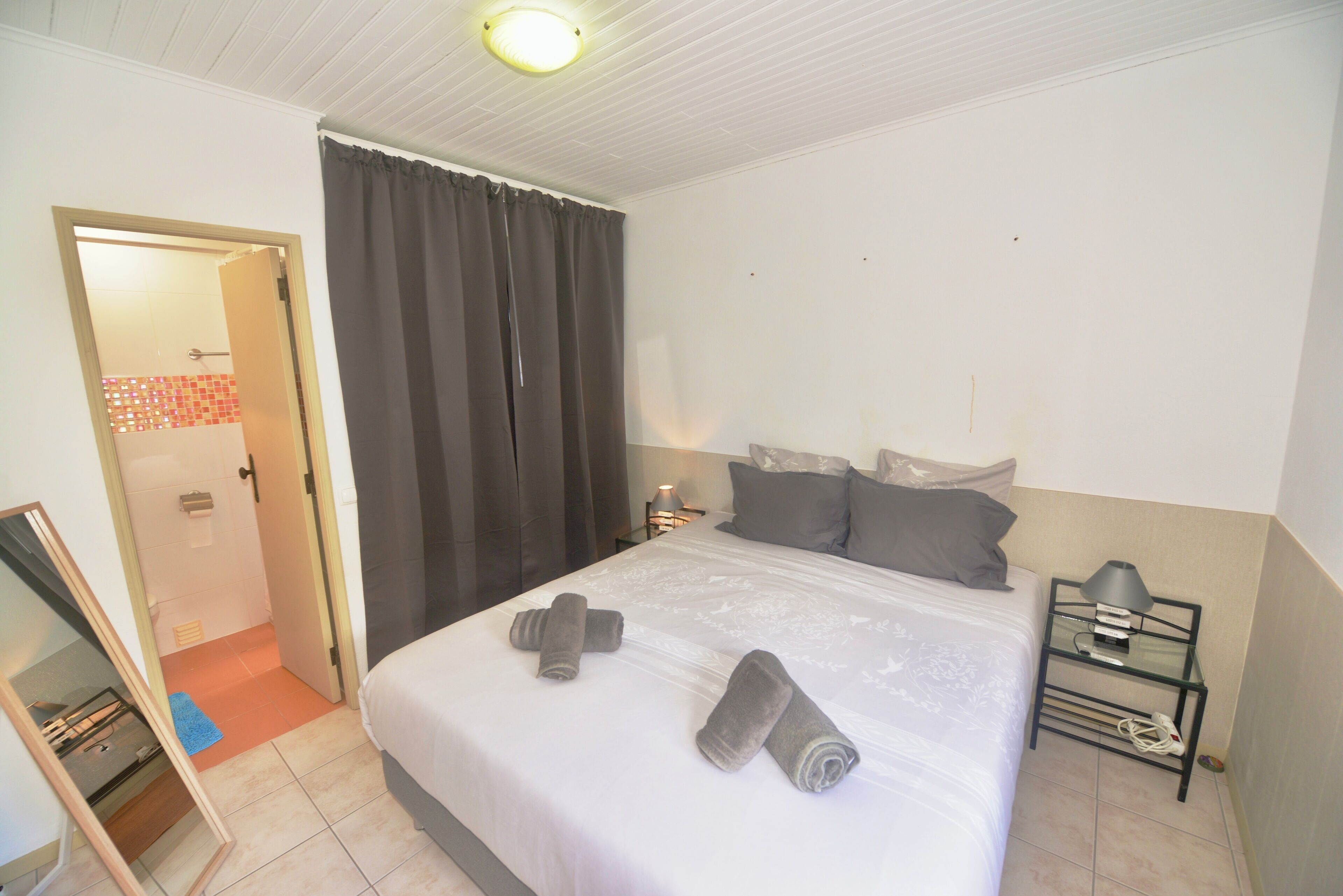 A hotel room with a bed, a nightstand, a lamp, and a door leading to a bathroom.