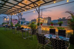 An outdoor dining area with tables and chairs, surrounded by greenery and potted plants.