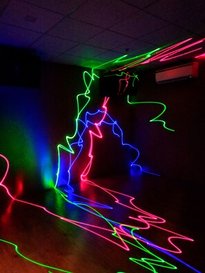 Ein Zimmer mit dunklem Boden und bunten Neonlicht-Mustern an der Decke.