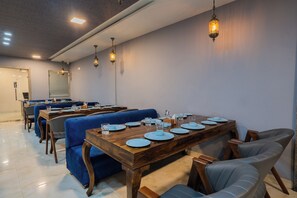 A dining area with wooden tables, blue upholstered chairs, and hanging pendant lights. - The Raas Mahal (Jaipur)