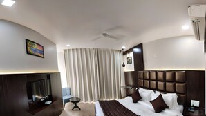 Una habitación de hotel moderna con una cama curvada, un televisor de pantalla plana montado en la pared, una mesita redonda pequeña y un ventilador de techo.