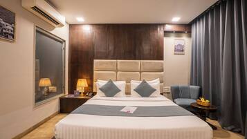 A hotel room with a large bed, a bedside table with a lamp, a chair, and a small table with fruit.