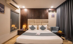 Une chambre d’hôtel avec un grand lit, une table de chevet avec une lampe, une chaise et une petite table avec des fruits.