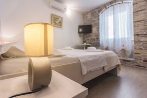 A hotel room with a bed, a bedside lamp, a television on the wall, and a stone wall. - Apartments Centrum Split (Split)